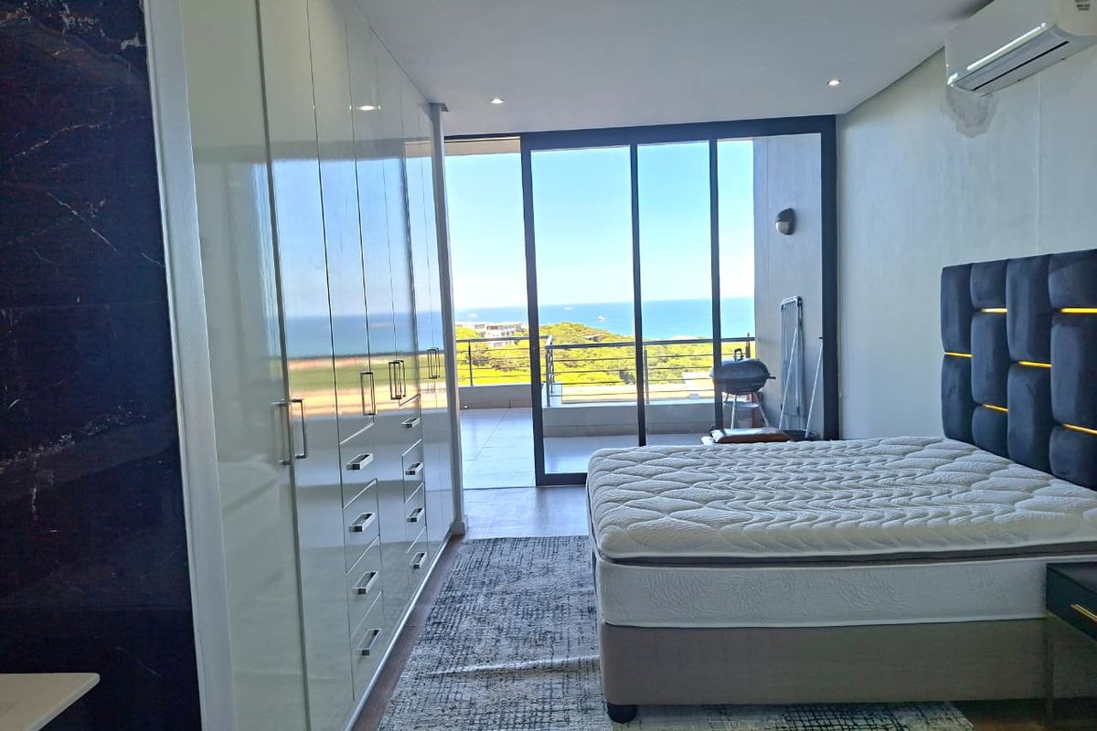 Modern bedroom featuring extensive built-in cupboards, air conditioning, and large sliding doors opening onto a balcony with scenic ocean views.