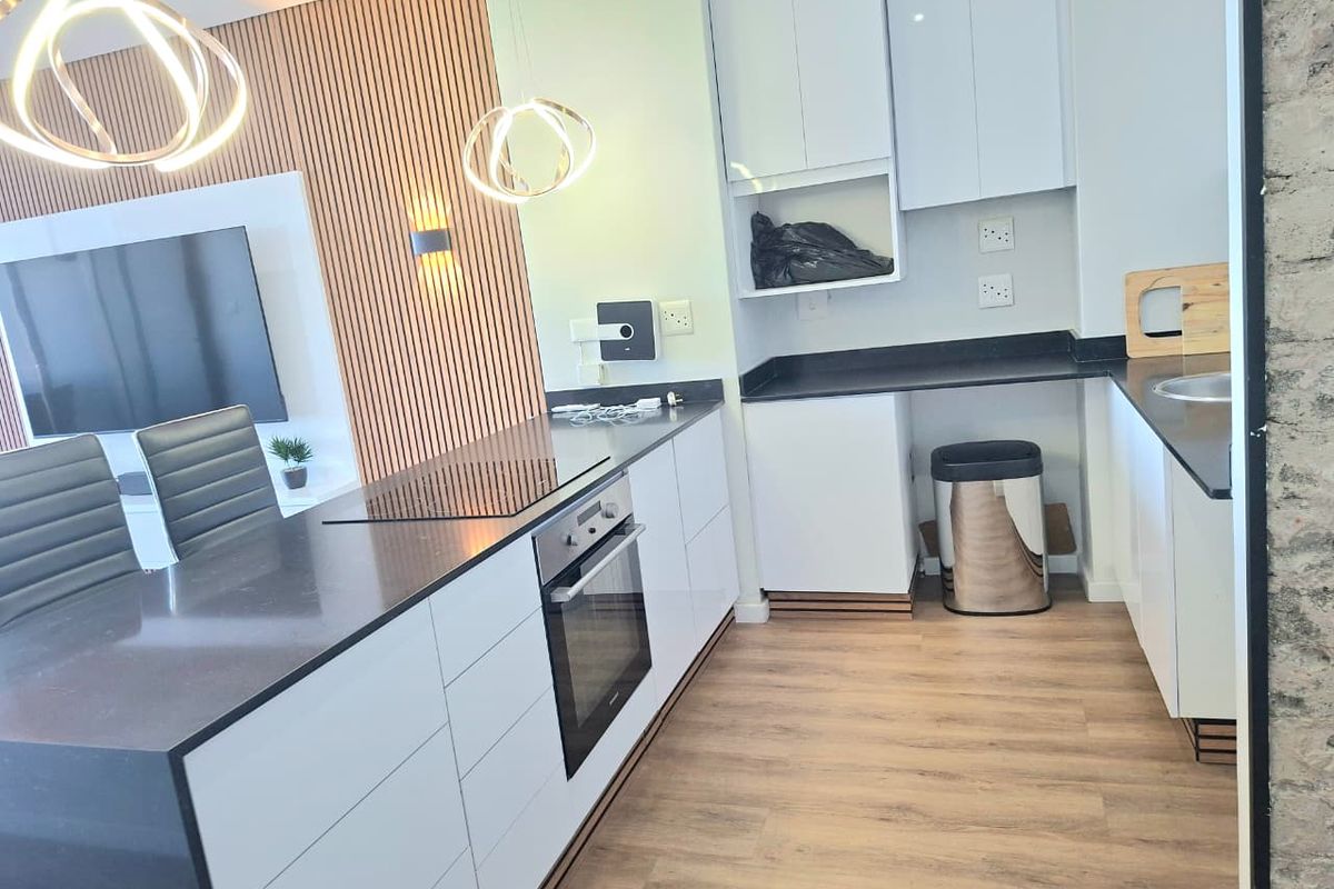 Modern open-plan kitchen and living area featuring sleek white cabinetry, dark stone countertops, built-in oven, and a stylish slatted wood feature wall.