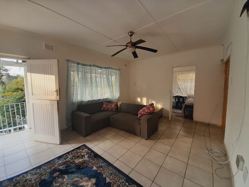 A living room featuring tiled flooring, a ceiling fan, and direct access to a balcony through a door.