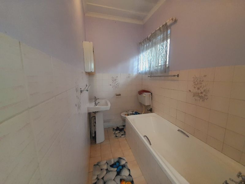 A dated bathroom featuring a standard bathtub, pedestal basin, and toilet with original ceramic wall tiling and floor finishes.