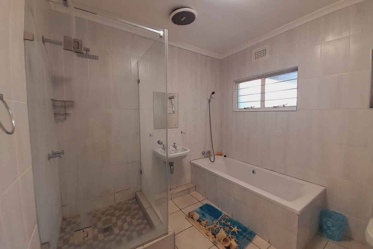 A functional bathroom featuring a glass-enclosed shower, a built-in bathtub, and a wall-mounted basin with tiled finishes throughout.