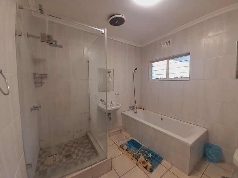 A functional bathroom featuring a glass-enclosed shower, a built-in bathtub, and a wall-mounted basin with tiled finishes throughout.
