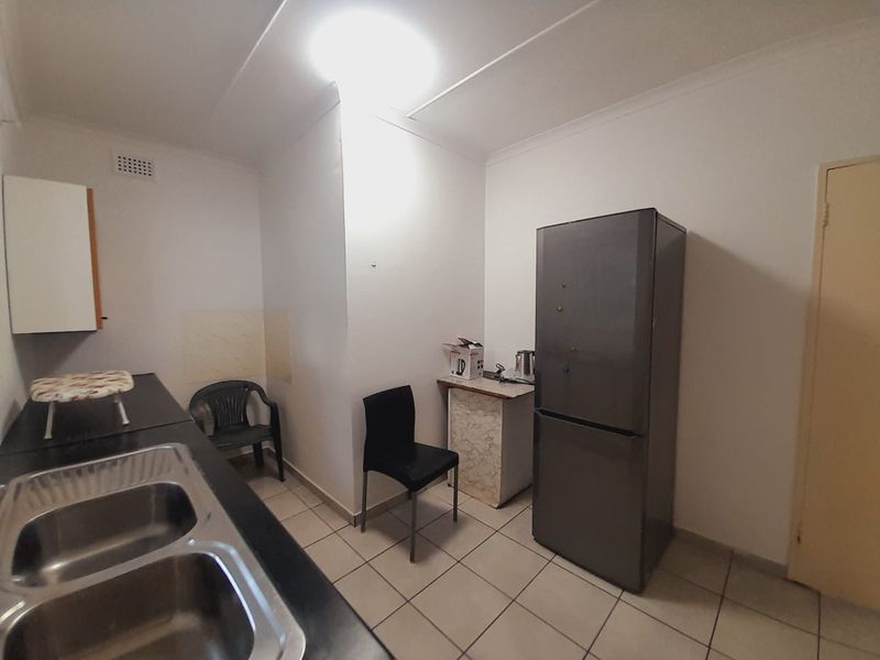 A functional kitchen area featuring a double bowl stainless steel sink, tiled flooring, and basic cabinetry, offering potential for modernization and layout optimization.