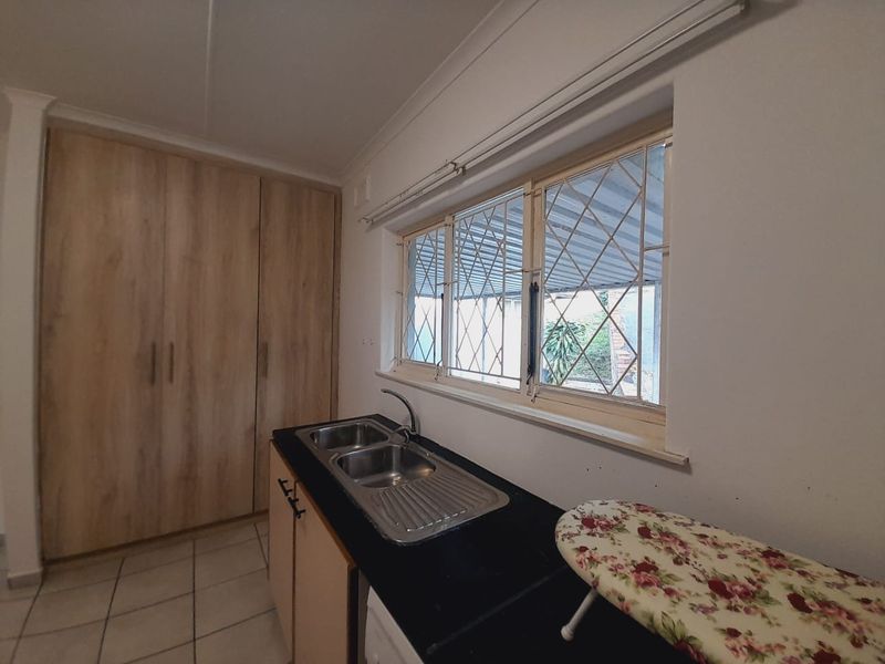 Functional laundry area featuring built-in cabinetry, a stainless steel double sink, and tiled flooring with security bars on the window.