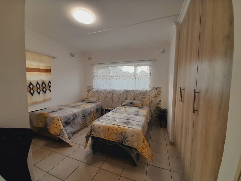 A functional bedroom featuring tiled flooring, built-in wooden cupboards, and a window with natural light.