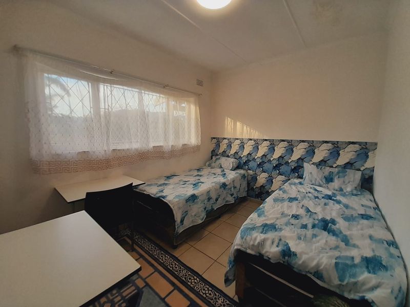 A bedroom featuring tiled flooring and security bars on the window, currently configured with twin beds and dated wall treatments.
