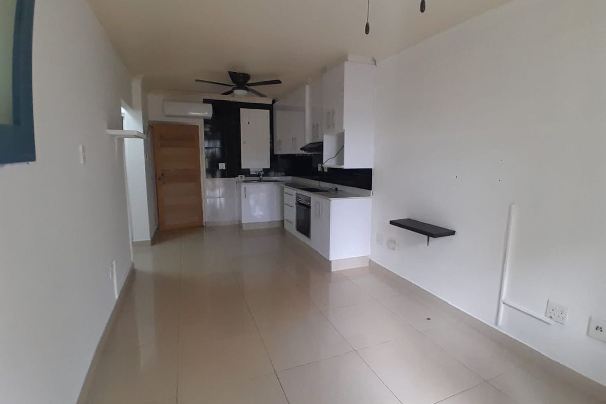 An open-plan living and kitchen area featuring white cabinetry, built-in appliances, tiled flooring, and an integrated air conditioning unit.