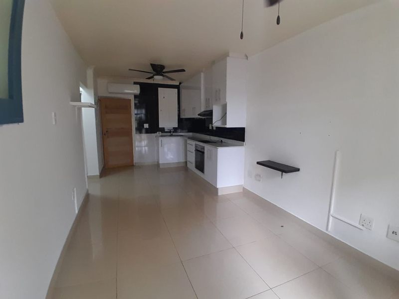 An open-plan living and kitchen area featuring white cabinetry, built-in appliances, tiled flooring, and an integrated air conditioning unit.