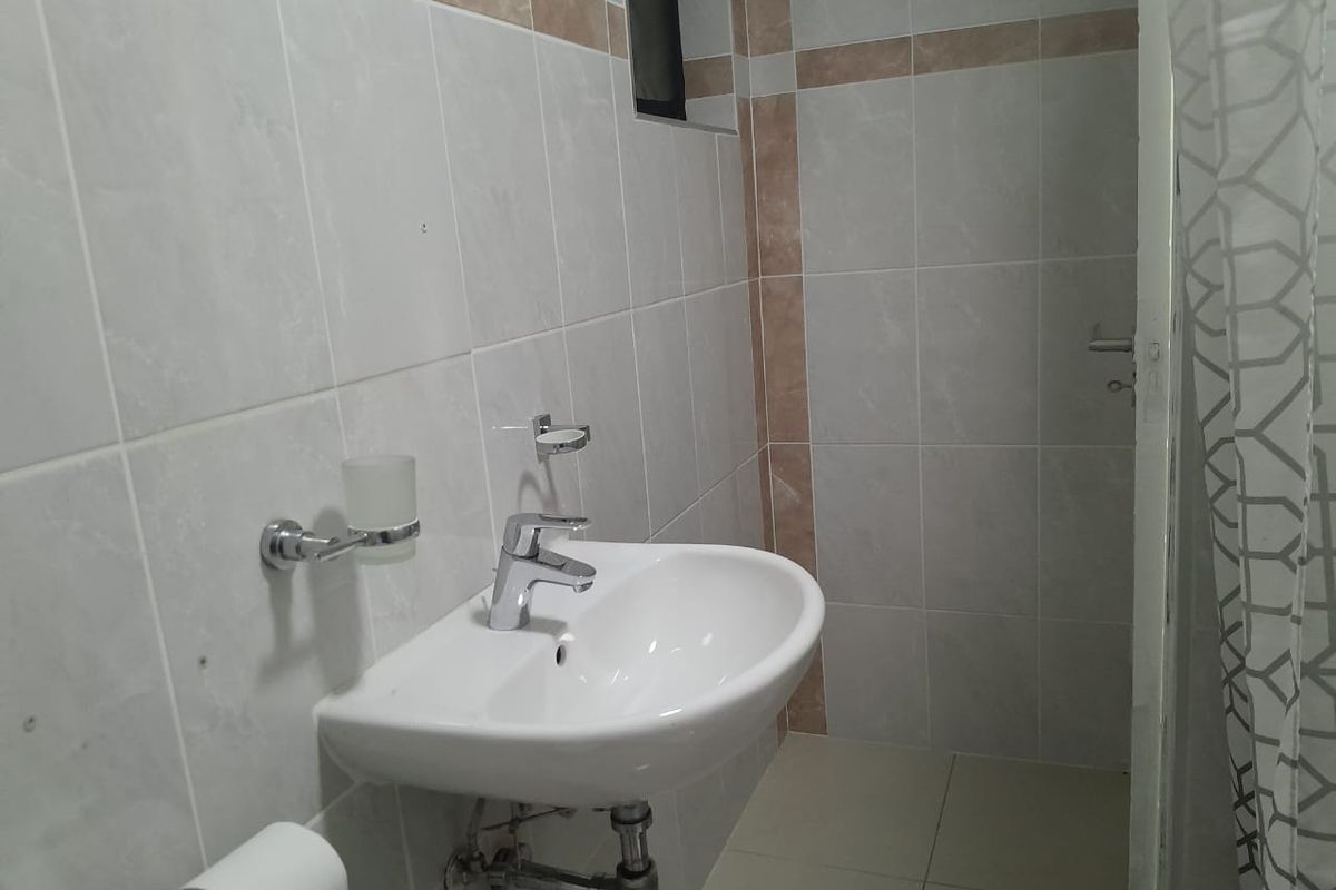 A functional bathroom featuring a wall-mounted basin with chrome fixtures and neutral ceramic wall and floor tiling.