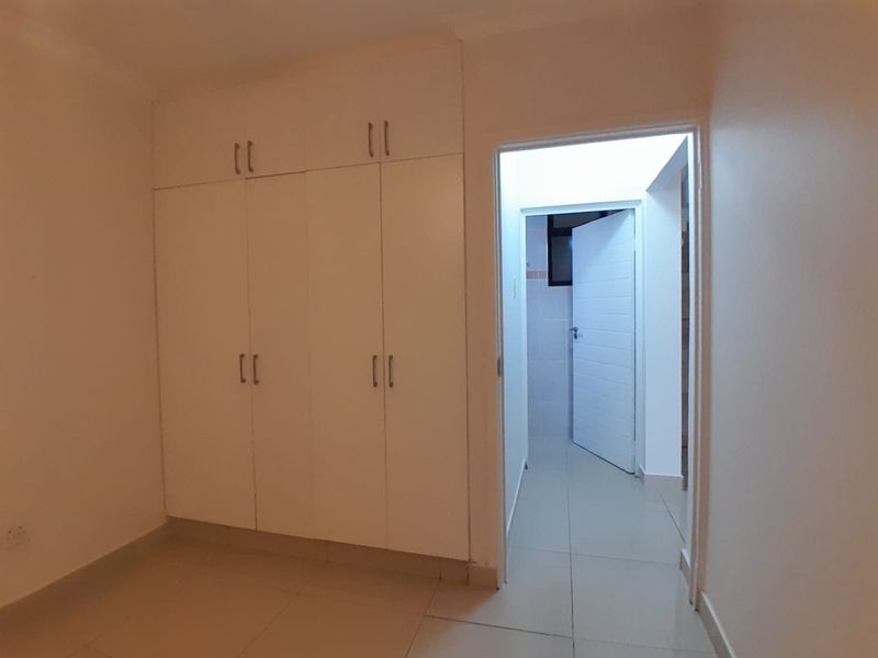 A clean, empty bedroom featuring neutral tiled flooring and ample built-in cupboard storage, leading into an adjacent hallway area.