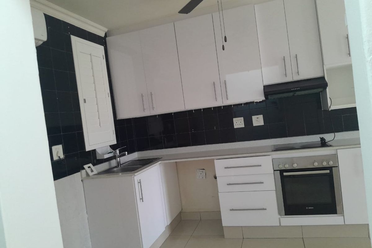 A functional kitchen featuring white gloss cabinetry, a black tiled backsplash, built-in oven, hob, and extractor fan, with tiled flooring throughout.