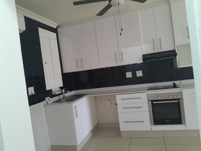 A functional kitchen featuring white gloss cabinetry, a black tiled backsplash, built-in oven, hob, and extractor fan, with tiled flooring throughout.