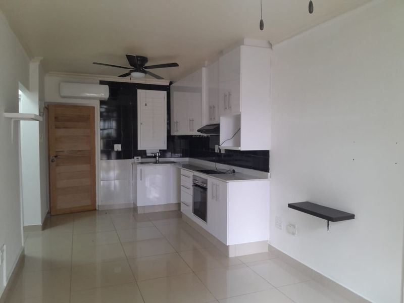 A clean, modern kitchen featuring white cabinetry, integrated appliances, tiled flooring, and a black tiled backsplash, offering a functional and bright cooking space.