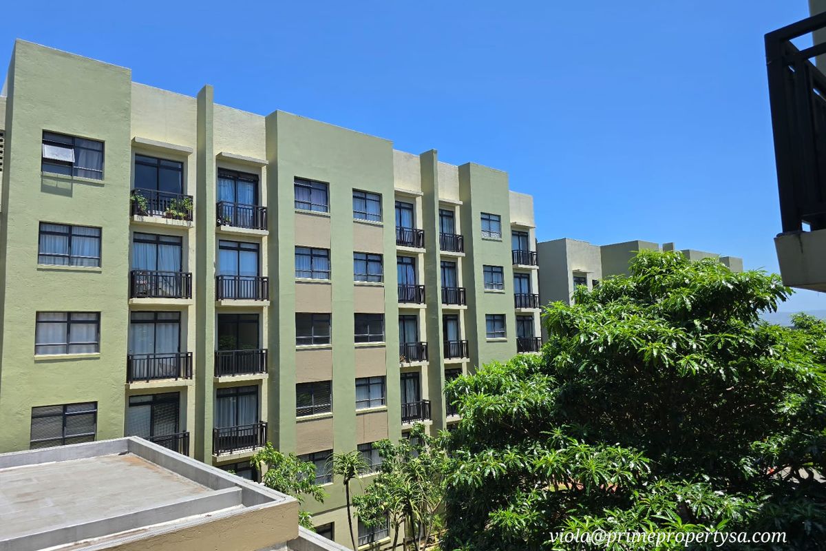 Exterior view of a multi-story apartment building featuring a green facade, uniform balcony structures, and aluminium-framed windows set against a clear blue sky.