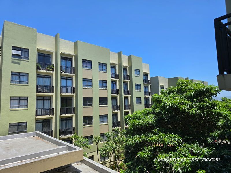Exterior view of a multi-story apartment building featuring a green facade, uniform balcony structures, and aluminium-framed windows set against a clear blue sky.