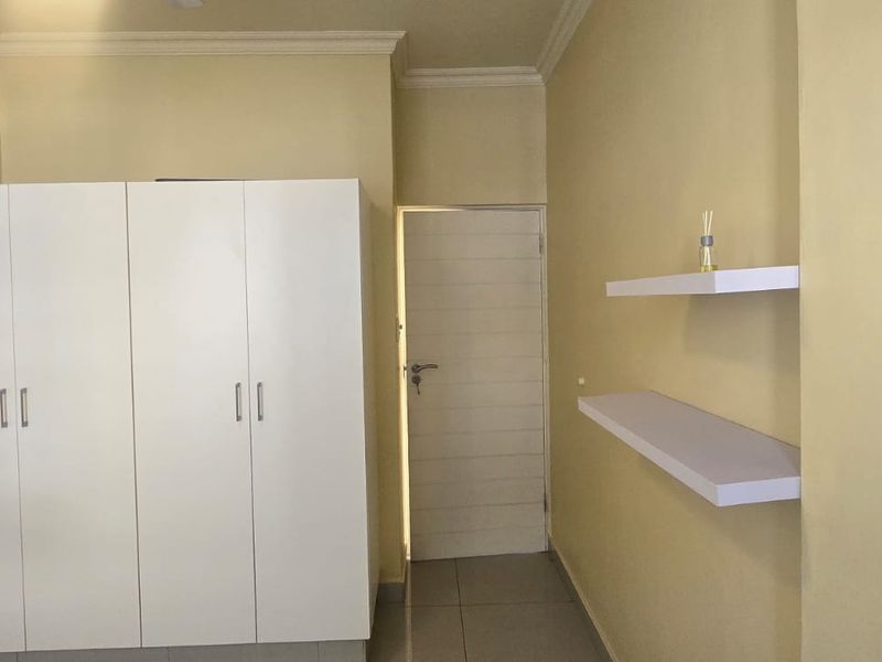A bedroom featuring a white built-in wardrobe, floating wall shelves, and neutral tiled flooring with decorative ceiling cornicing.