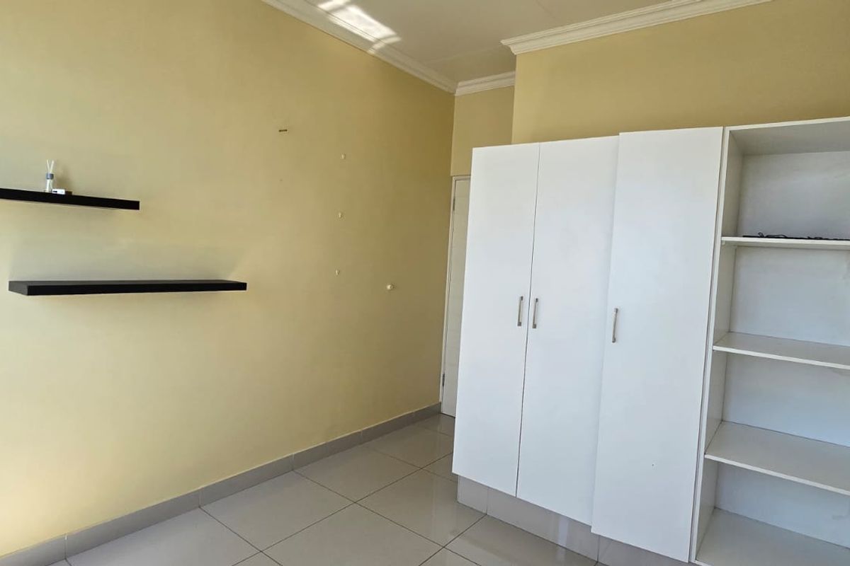 A bedroom featuring tiled flooring, built-in white wardrobe cabinetry, and wall-mounted floating shelves.