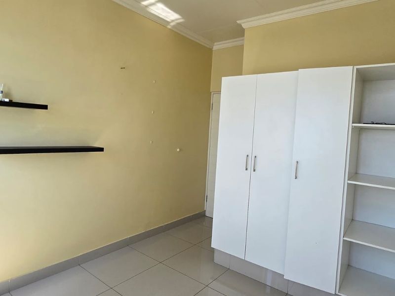 A bedroom featuring tiled flooring, built-in white wardrobe cabinetry, and wall-mounted floating shelves.