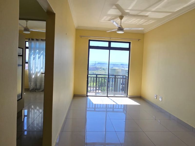 A bright, empty living room featuring tiled floors, a ceiling fan, and a sliding glass door leading to a balcony with scenic views.