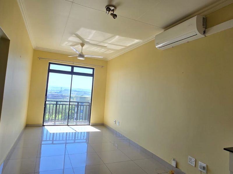 An open-plan living area featuring tiled floors, a ceiling fan, split-system air conditioning, and access to a balcony with scenic views.