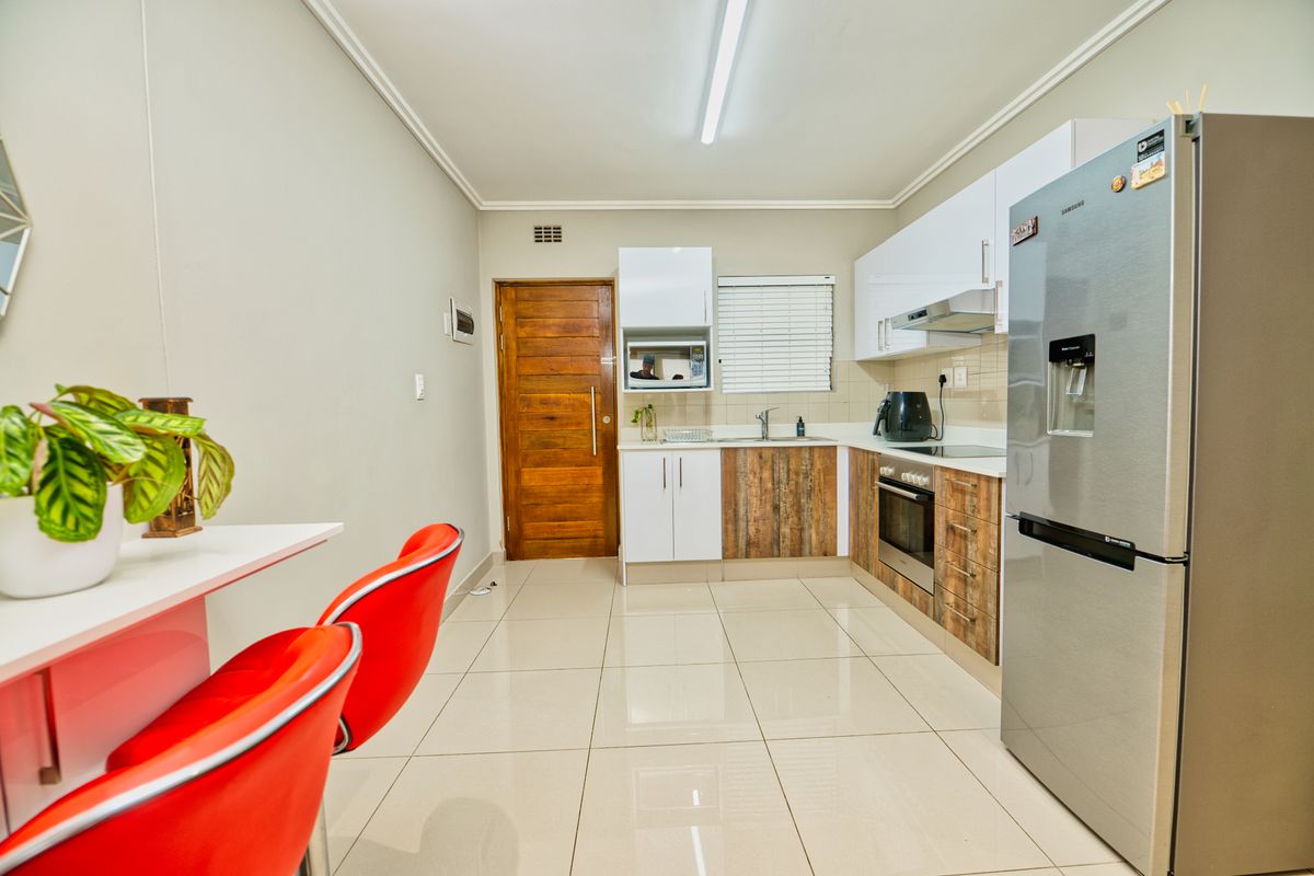 Modern kitchen featuring a mix of white and wood-grain cabinetry, stainless steel appliances, tiled flooring, and a breakfast bar area.