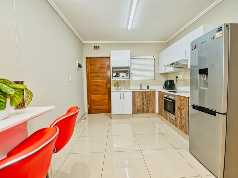 Modern kitchen featuring a mix of white and wood-grain cabinetry, stainless steel appliances, tiled flooring, and a breakfast bar area.