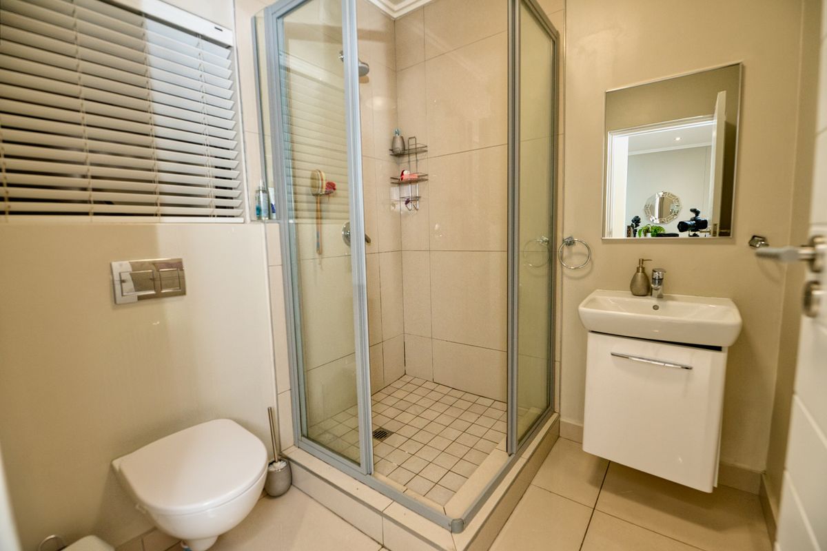 Modern bathroom featuring a glass-enclosed shower, wall-mounted toilet, and a sleek vanity basin with neutral wall and floor tiling.