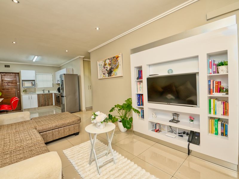 Open-plan living area featuring a modern built-in media unit, tiled flooring, and a functional kitchen with integrated cabinetry and appliances.