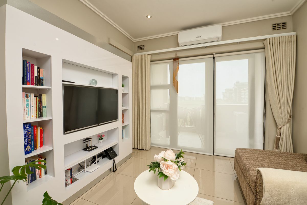 A well-maintained living room featuring a modern built-in media and shelving unit, tiled floors, and large sliding doors leading to a balcony.
