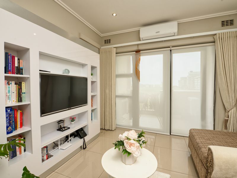 A well-maintained living room featuring a modern built-in media and shelving unit, tiled floors, and large sliding doors leading to a balcony.