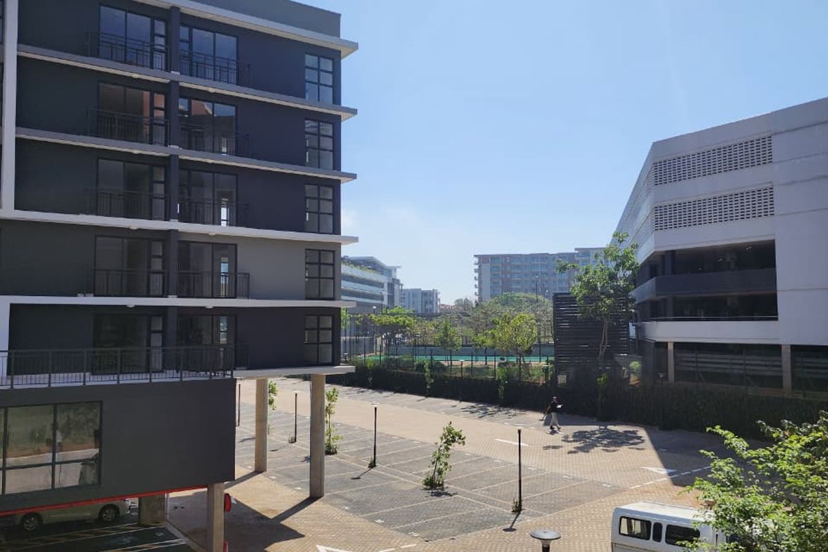 An elevated view of the apartment complex grounds, featuring paved parking bays, modern building facades, and surrounding infrastructure.