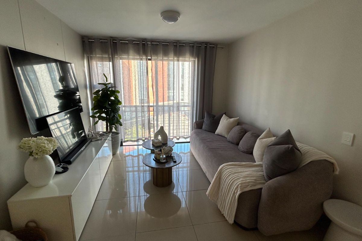 A well-maintained living room featuring polished tiled flooring and a large sliding glass door providing access to the balcony.