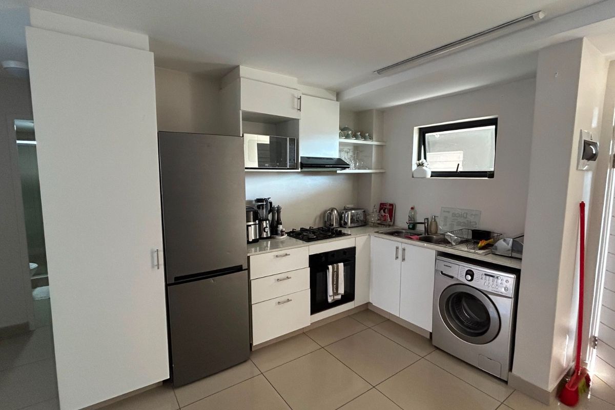 Compact modern kitchen featuring white cabinetry, integrated appliances including a gas hob, oven, and built-in microwave, with tiled flooring throughout.