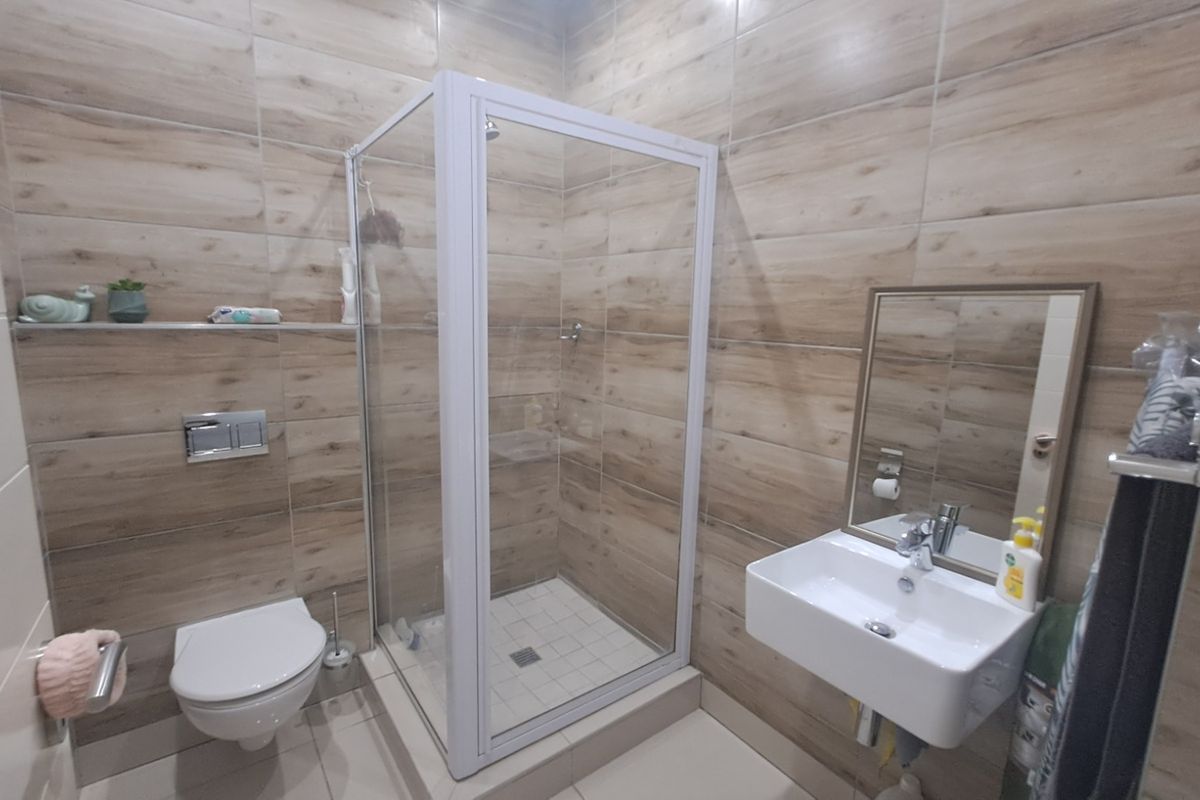Modern bathroom featuring a glass shower enclosure, wall-mounted basin, and wall-mounted toilet with contemporary wood-look wall tiling.