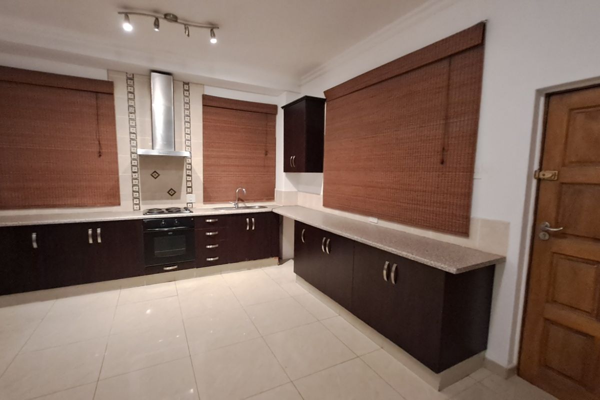 A spacious kitchen featuring dark wood cabinetry, stone countertops, built-in oven with extractor fan, and tiled flooring.