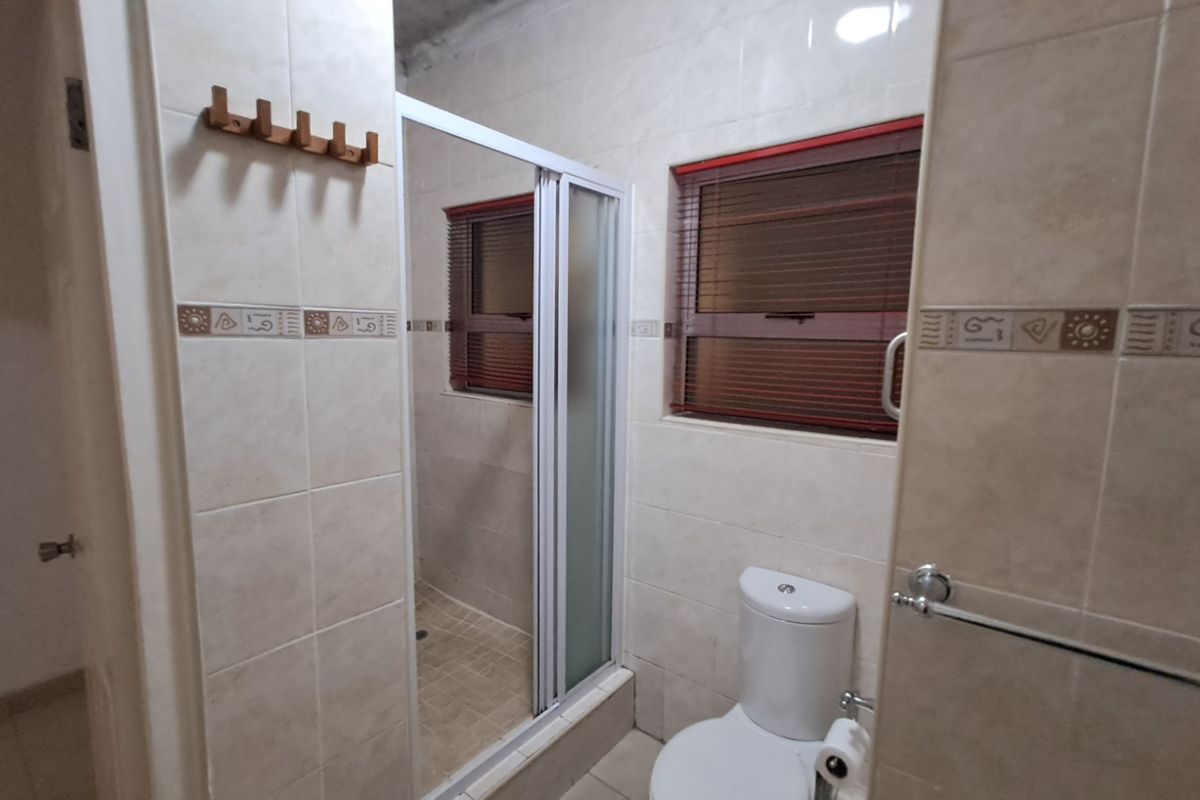A functional bathroom featuring a shower enclosure, toilet, and neutral wall tiling with decorative accents.