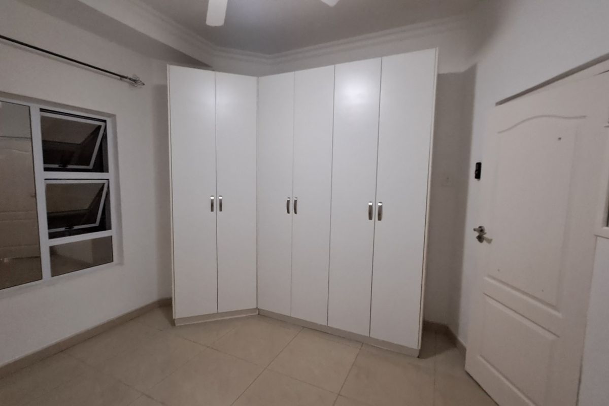 A clean, empty bedroom featuring neutral tiled flooring, white built-in cupboards, and a ceiling fan, offering a blank canvas for personalization.