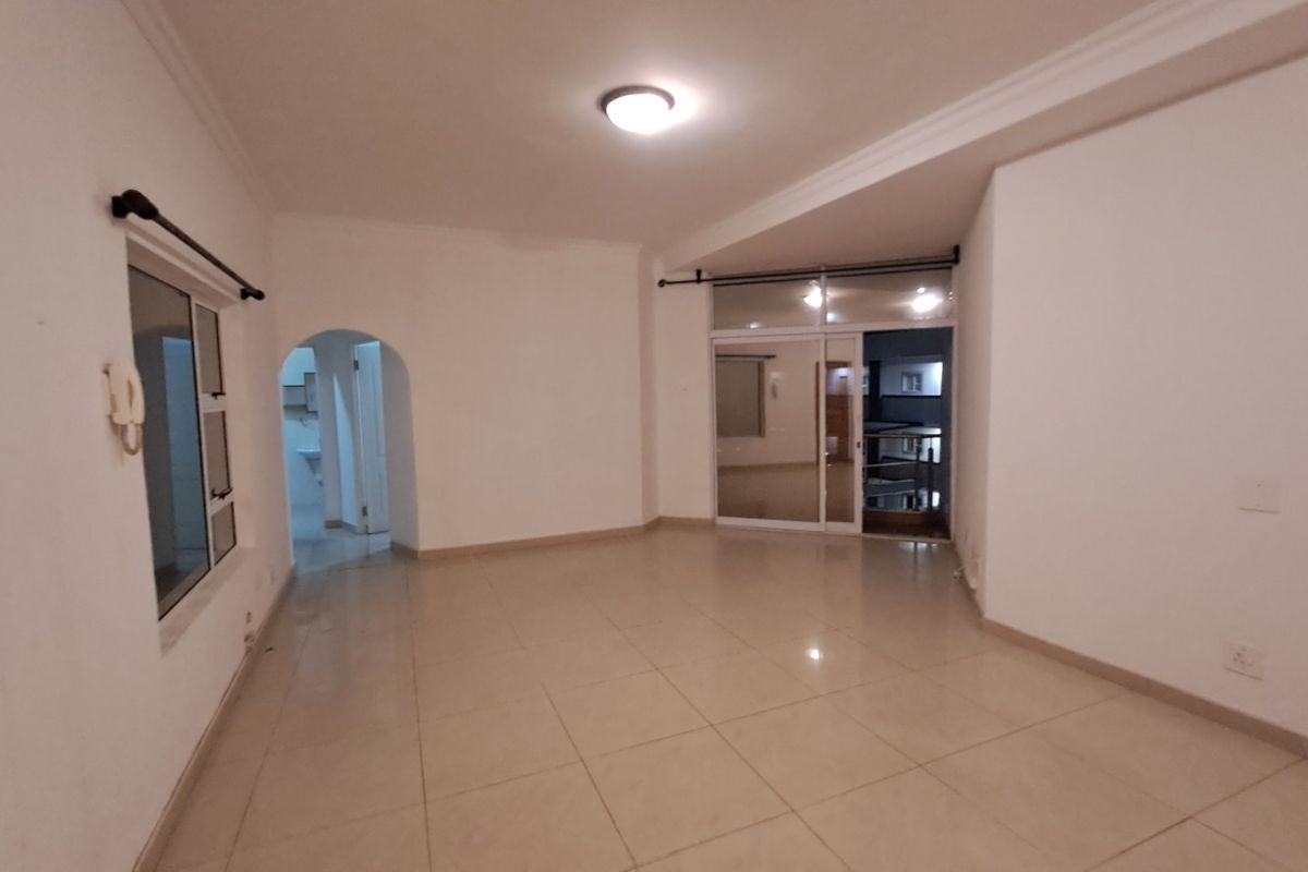 A spacious, empty living area featuring neutral tiled flooring, an arched entryway, and a sliding glass door leading to an outdoor space.