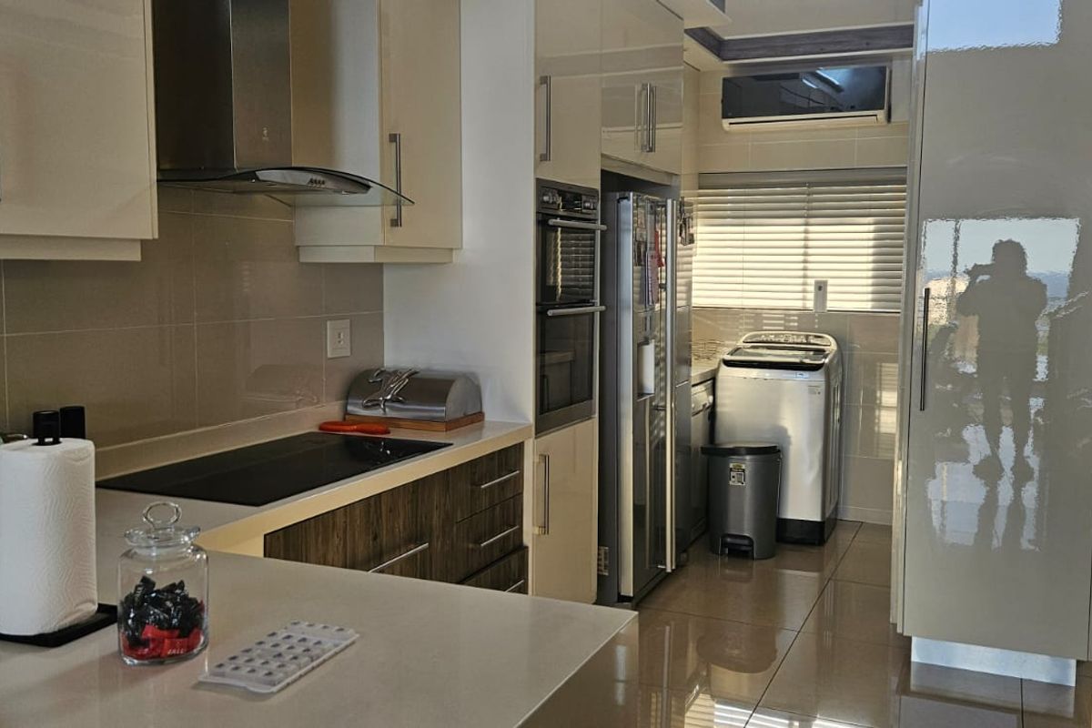 Modern kitchen featuring high-gloss cabinetry, stone countertops, integrated appliances, and tiled flooring, offering a sleek and functional culinary space.