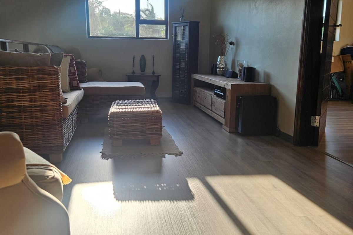A living room area featuring light-toned laminate flooring and aluminium window frames, offering a functional space with natural light.