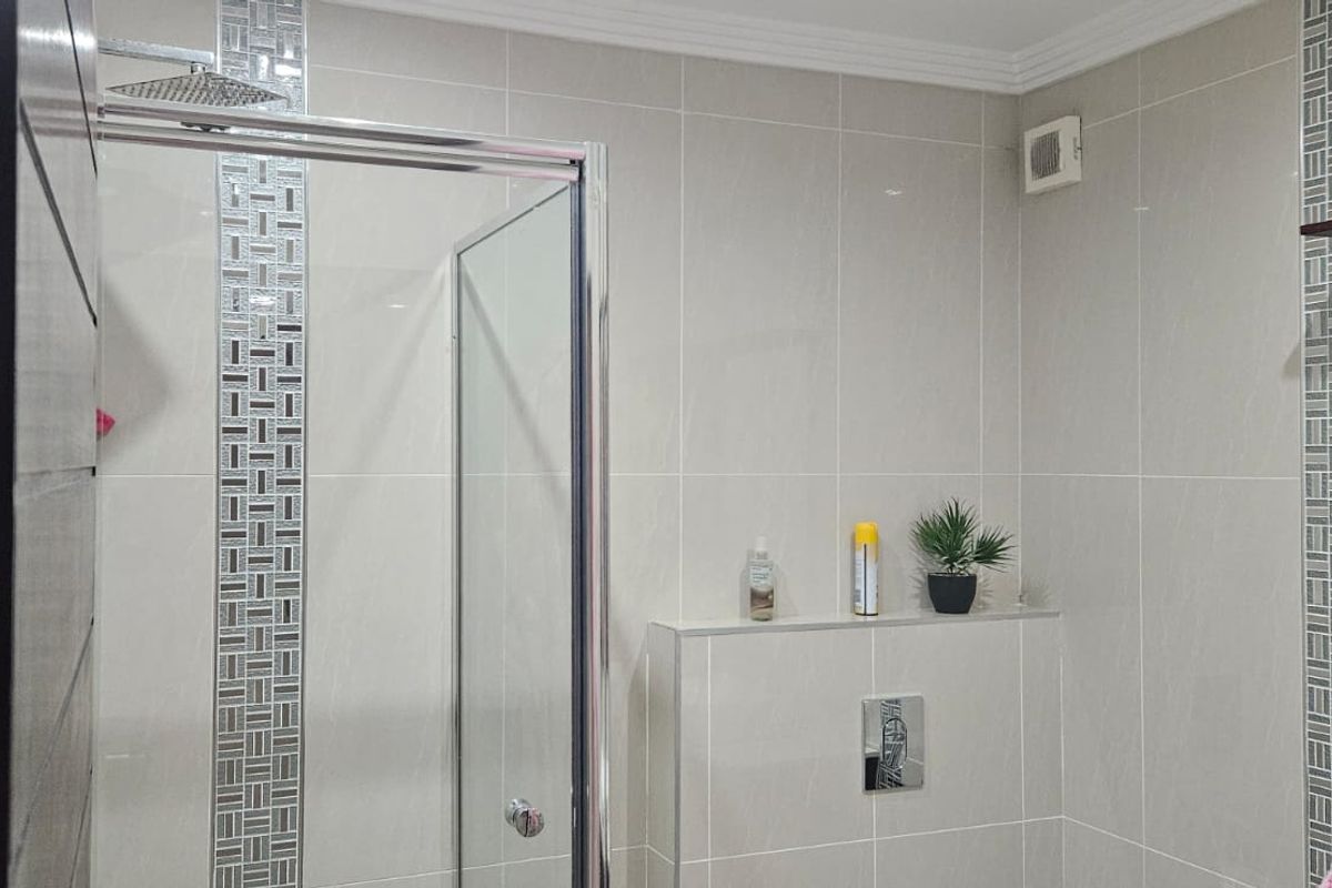 Modern bathroom featuring a glass-enclosed shower with a rainfall shower head and decorative mosaic tile accents.