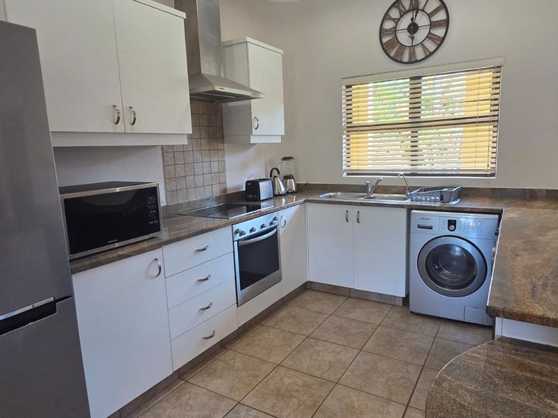 A functional kitchen featuring granite countertops, white cabinetry, built-in oven, electric hob, extractor fan, and a double sink with tiled backsplash.