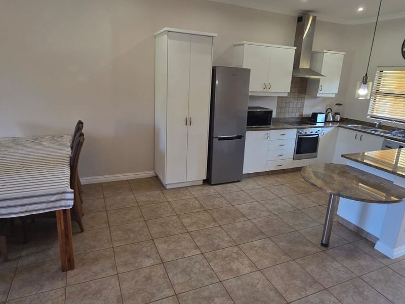 Open-plan kitchen and dining area featuring tiled flooring, white cabinetry, stainless steel appliances, and a breakfast counter.