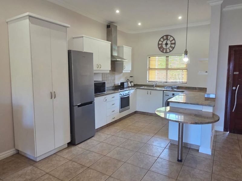 A functional kitchen featuring white cabinetry, granite countertops, a breakfast nook, and built-in appliances, finished with tiled flooring and recessed lighting.