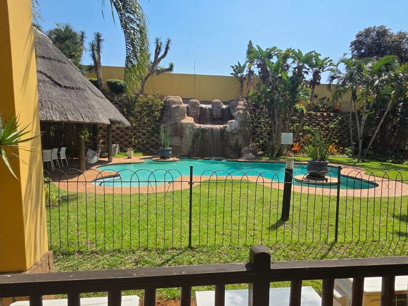 Outdoor pool area featuring a rock waterfall, landscaped garden, and a thatched lapa, providing a private and tranquil entertainment space.