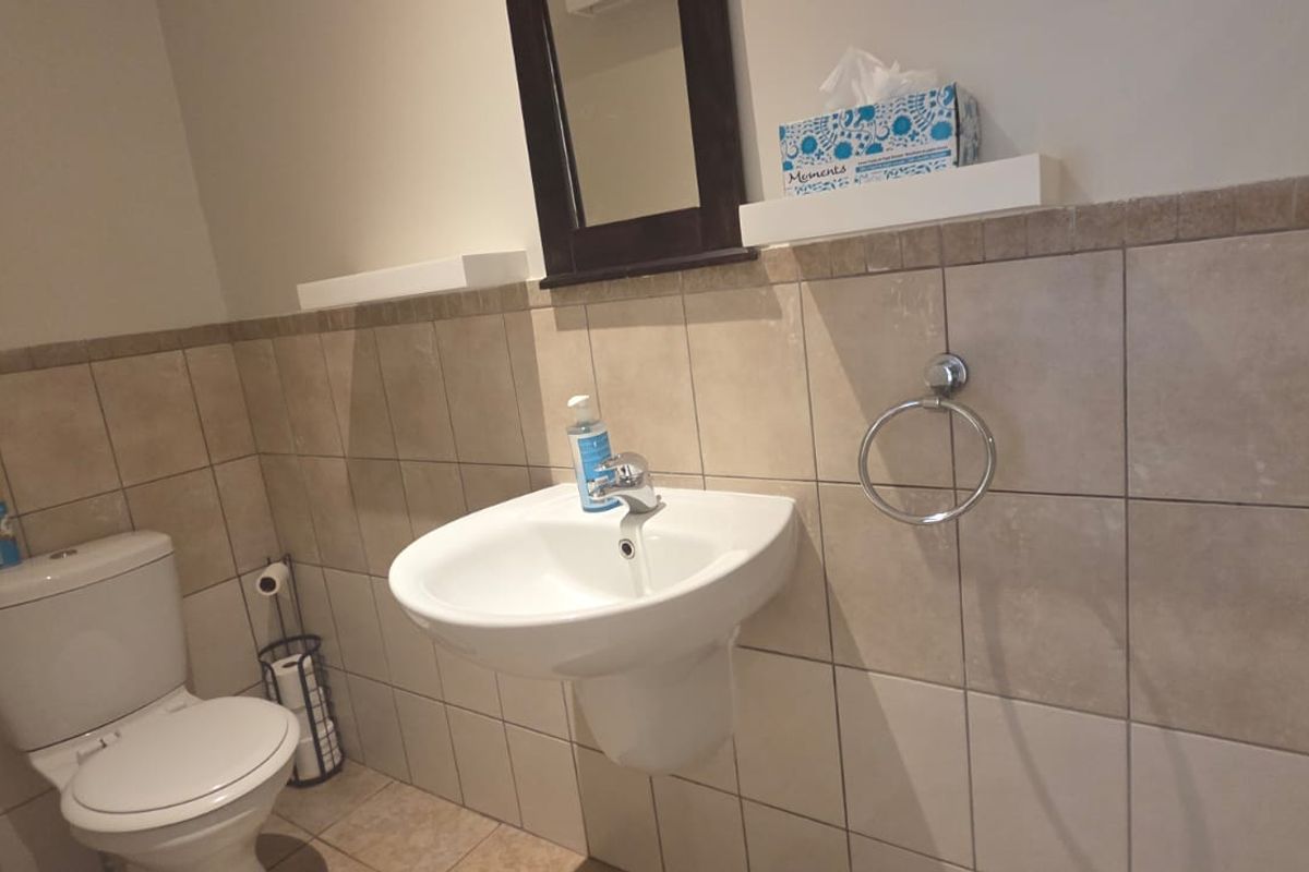 A functional bathroom featuring a wall-mounted basin, toilet, and neutral tiled walls with floating shelving.