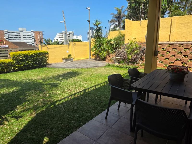 A covered patio area overlooking a private garden with a lawn, wooden deck section, and secure perimeter walling with electric fencing.