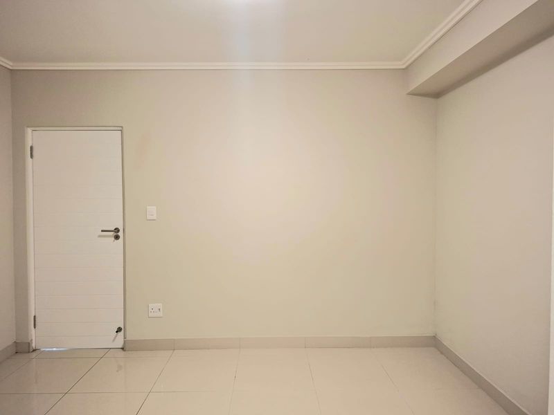 A clean, empty bedroom featuring neutral wall paint, tiled flooring, and a modern internal door, providing a blank canvas for personalization.