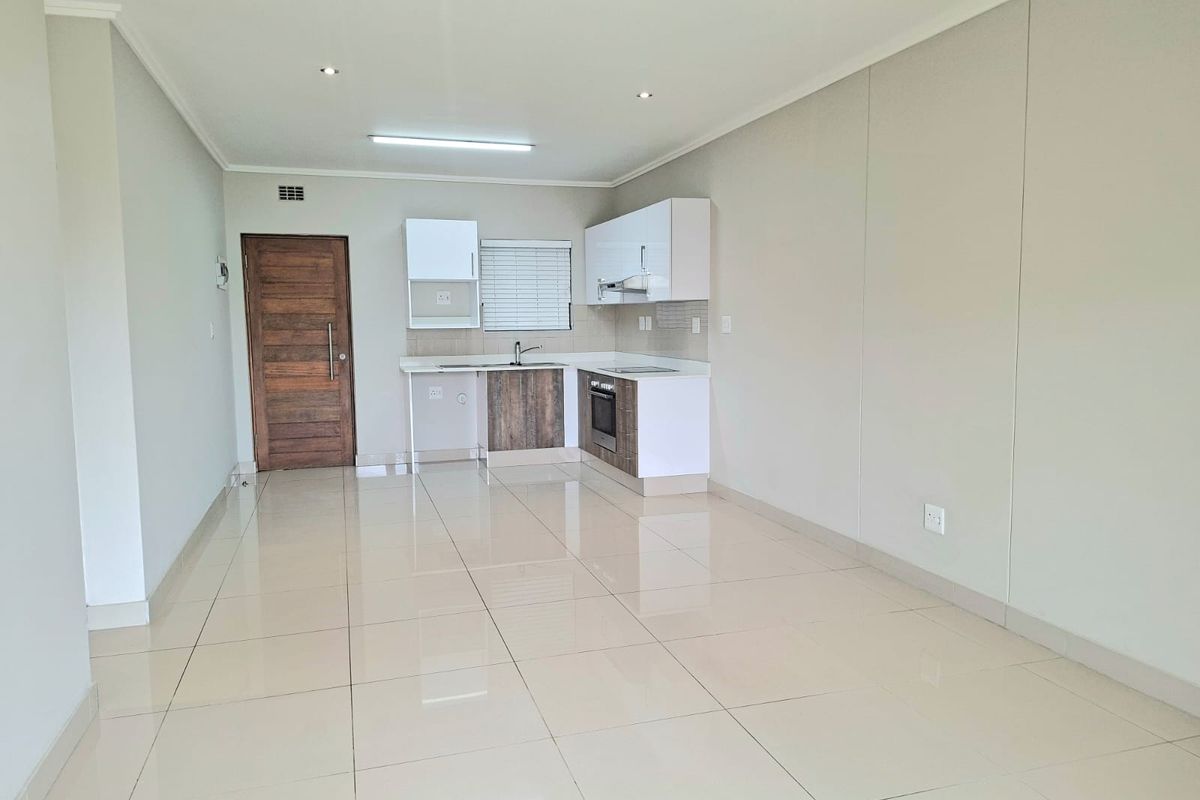 Modern open-plan living area featuring a compact kitchen with built-in cabinetry, oven, hob, and sleek tiled flooring throughout.