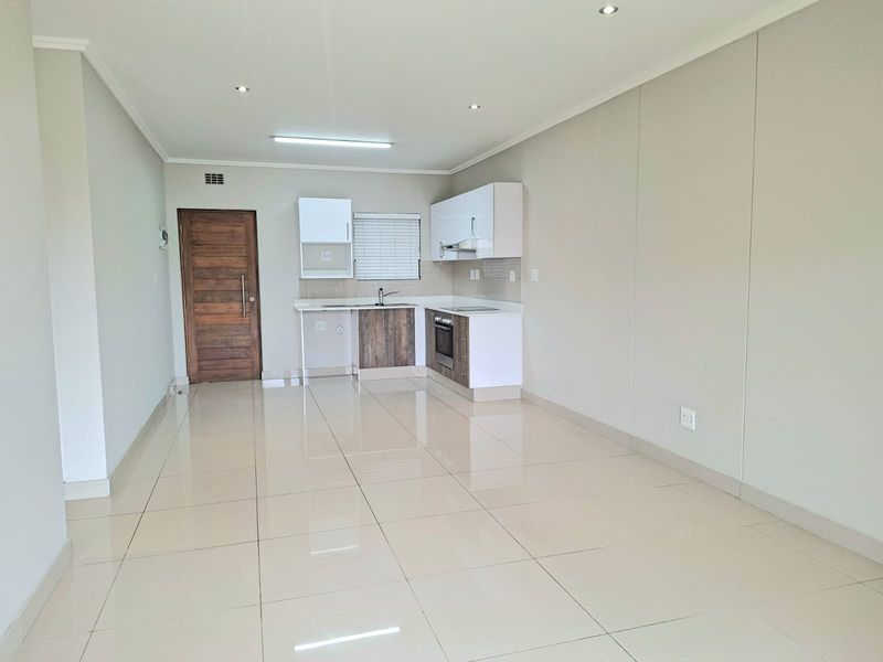 Modern open-plan living area featuring a compact kitchen with built-in cabinetry, oven, hob, and sleek tiled flooring throughout.